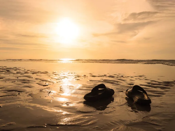 Silhueta sandálias pretas na areia na praia dourada do pôr do sol . — Fotografia de Stock