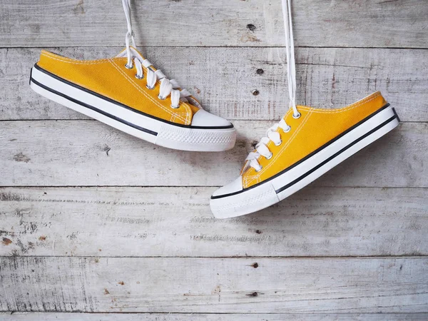 Gelbe Turnschuhe mit weißem Schnürsenkel, die über Vintage-Schuhen hängen — Stockfoto