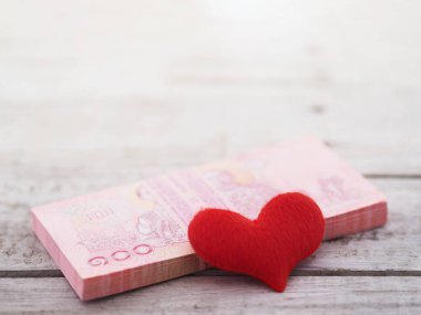 Tahta masa arkasında 100 baht ve kalp şeklinde Tayland banknotları yığını kapatın. Alışverişe bayılırım..