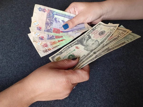 women hands exchanging Belizean banknotes and American dollar money