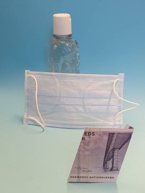 Danimarka banknotu 50 kron, yüz maskesi, jel alkollü şişe ve mavi arka plan.