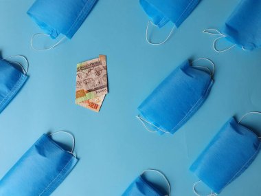 Maske ve 20 dolarlık banknot mavi arka planda.