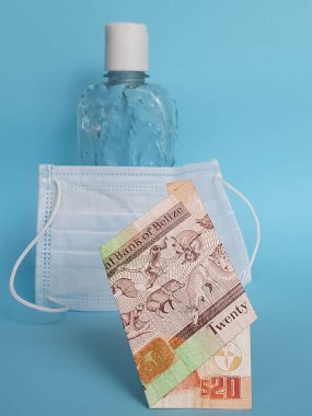 20 dolarlık Belizean banknotu, yüz maskesi, jel alkollü şişe ve mavi arka plan.