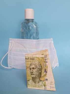 Tunus banknotu beş dinar, yüz maskesi, jel alkollü şişe ve mavi arka plan