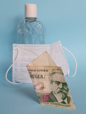 Uruguaylı banknot. 20 peso, yüz maskesi, jel alkollü şişe ve mavi arka plan.