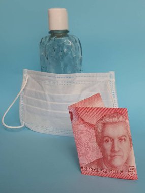 Şili banknotu 5000 peso, yüz maskesi, jel alkollü şişe ve mavi arka plan