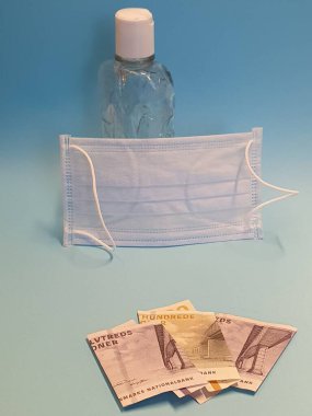 Danimarka banknotları, yüz maskesi, jel alkollü şişe ve mavi arka plan.