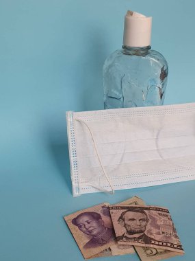 Amerikan 5 dolarlık banknot, Çin banknotu 5 yuan, yüz maskesi, jel alkollü şişe ve mavi arka plan.