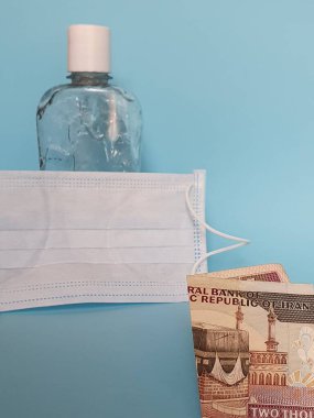 2000 riyal, yüz maskesi, jel alkollü şişe ve mavi arka plan İran banknotları.