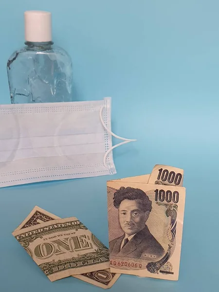 american one dollar bill, japanese banknote of 1000 yen, face mask, bottle with gel alcohol and blue background