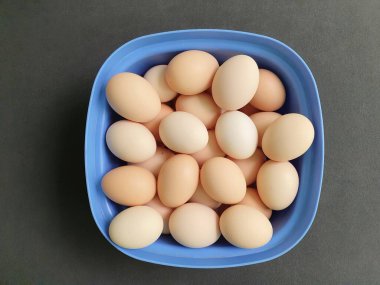Mavi plastik bir kapta taze organik yumurta yığını.