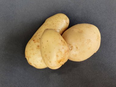 Siyah yüzeyde üç parça taze patates sebzesi, yukarıdan görünüyor.