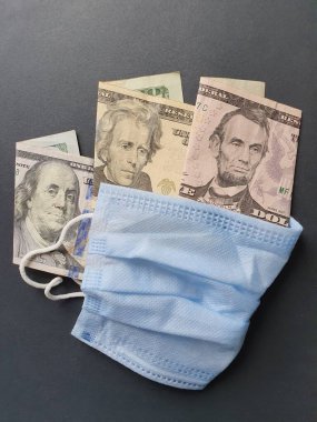 Mavi tek kullanımlık maske ve farklı değerlerde Amerikan doları banknotları.