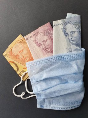 Tek kullanımlık mavi maske ve farklı değerlerde Brezilya banknotları.
