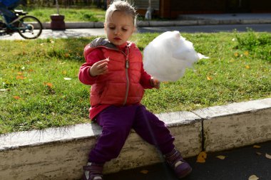 İfade dolu yüzü olan küçük güzel kız parkta pamuk şeker yiyor.