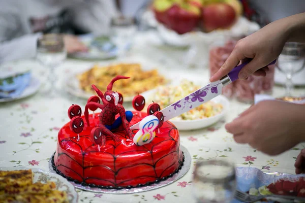 a hand cuts a cake in the shape of spider man