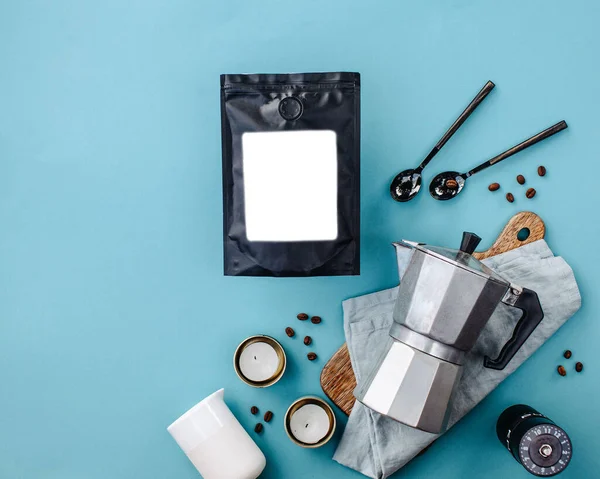 coffee bag with a white label, geyser coffee machine and coffee beans on a blue background flatlay