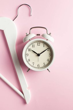  Pembe arka planda çalar saat ve elbise askısı var. Alışveriş konsepti, kıyafet alışverişi, indirimlerin ve satışların başlangıcı, gardırop analizi zamanı, stilistler. Boşluğu kopyala.