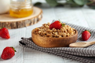 Beyaz ahşap zemin üzerinde çilek ve bal bulunan ahşap bir kasede ev yapımı tahıl gevreği. Sağlıklı kahvaltı kavramı..