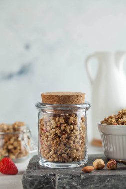 Tahta bir tahtanın üzerinde cam bir kavanozda fındıklı ve çilekli ev yapımı granola. Hızlı ve sağlıklı kahvaltı konsepti, vejetaryen kahvaltısı.