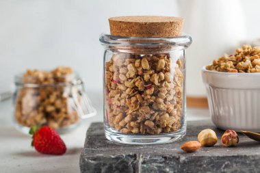  Tahta bir tahtanın üzerinde cam bir kavanozda fındıklı ve çilekli ev yapımı granola. Hızlı ve sağlıklı kahvaltı konsepti, vejetaryen kahvaltısı.