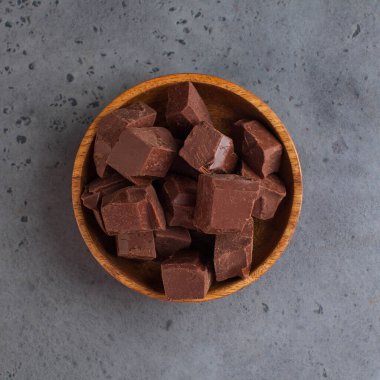 Süt çikolatası, gri arka planda tahta bir tabakta dilimlenir. Çiğ çikolata, sağlıklı tatlılar. Yemek fotoğrafı. Yüksek kalite fotoğraf