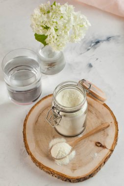 Tahta kaşıkta beyaz kolajen tozu, bir bardak su ve bir çiçek. Cilt bakımı, gençleştirme. Uzayı kopyala Yüksek kalite fotoğraf