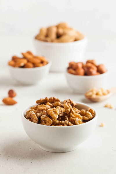 A handful of walnuts in a white bowl, assorted nuts on a light background. Healthy snacks, healthy fats. Copy space. High quality photo