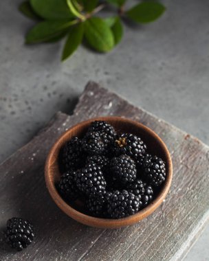 Gri arka planda tahta bir tabakta sulu olgun böğürtlenler. Koyu renk yemek fotoğrafı. Uzayı kopyala Yüksek kalite fotoğraf