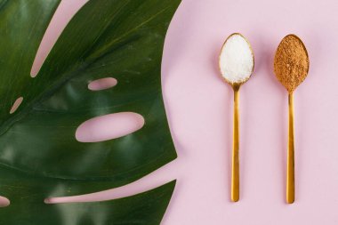 Hindistan cevizi ve saf beyaz şeker, pembe arka planda altın kaşıklarla. Minimalizm. Sağlıklı beslenme kavramı. Yüksek kalite fotoğraf.