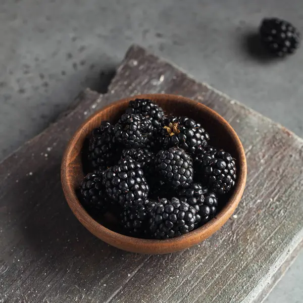 Gri arka planda tahta bir tabakta sulu olgun böğürtlenler. Koyu renk yemek fotoğrafı. Uzayı kopyala Yüksek kalite fotoğraf