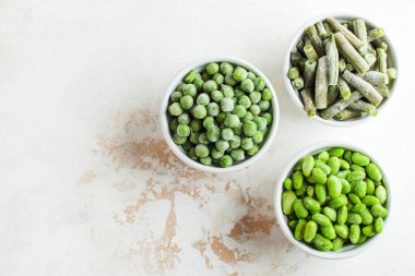 Donmuş sebzeler, taze bezelye, soya, yeşil fasulye ve beyaz kaselerde fotokopi alanı olan bebek maması. Sağlıklı yiyecek, donmuş yiyecek.