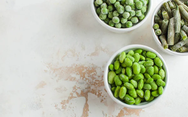 Замороженные овощи зеленый горошек, соя, зеленая фасоль и детское питание в белых мисках с пространством для копирования. Здоровые продукты питания, замороженные продукты — стоковое фото