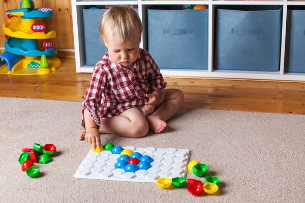 Un pequeño niño rubio lindo recoge mosaicos en el suelo en la habitación de los niños. Concepto de desarrollo infantil temprano. —  Fotos de Stock