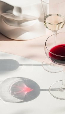 Sert ışıkta bir bardak şarap ve açık arkaplanda güzel uzun gölgeler. Moda fotoğrafları, minimalizm. Kutlama konsepti, yeni yıl, doğum günü. Uzayı kopyala Modern natürmort