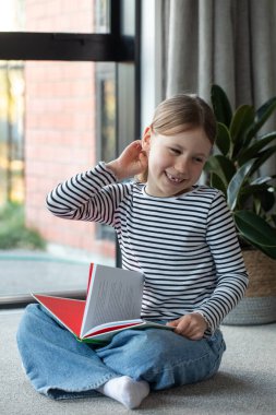 Evde rahat bir oturma odasında kitap okuyan mutlu bir çocuk. Eğitim kavramı