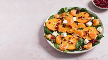 Taze hurma ve turunçgil salatası, ıspanak, feta ve pembe masada nar. Kış salatası. Noel salatası konsepti. Boşluğu kopyala
