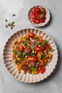 Taze nohut ve domatesli balkabağı salatası ve sağlıklı beslenmek için bitkiler. Sonbahar salatası. Sağlıklı ve vejetaryen yemeği kavramı.