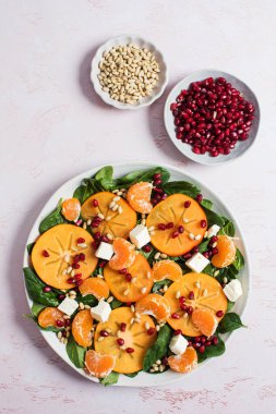 Taze hurma ve turunçgil salatası, ıspanak, feta ve pembe masada nar. Kış salatası. Noel salatası konsepti. 
