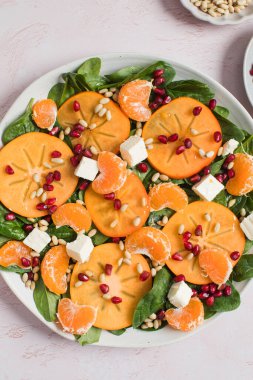 Taze hurma ve turunçgil salatası, ıspanak, feta ve pembe masada nar. Kış salatası. Noel salatası konsepti. 