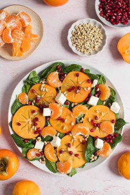 Taze hurma ve turunçgil salatası, ıspanak, feta ve pembe masada nar. Kış salatası. Noel salatası konsepti. 