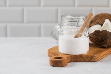 Creamy coconut yogurt on wooden board with half coconut and jar in kitchen setting. Concept of Vegan yogurt. Copy space