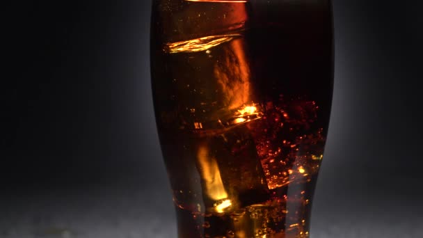 Glas mit Cola steht auf dem Tisch mit Eiswürfeln. Licht von hinten. Nahaufnahme — Stockvideo