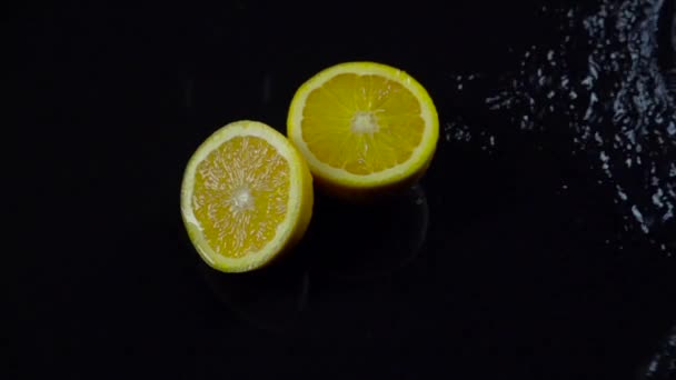 Halve sinaasappel met spatten van water op een zwarte achtergrond. Slow motion — Stockvideo