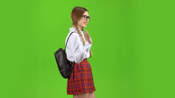 Schoolmeisje wandelingen met een rugzak op haar schouders en golven van haar hand. Groen scherm. Zijaanzicht — Stockvideo