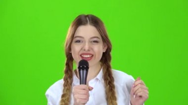 Kız öğrenci içine belgili tanımlık mikrofon ve gülümsüyor söylüyor. Yeşil ekran