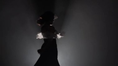 Şapkalı bir kadın Arjantinli dans kastanyet ile dans ediyor. Arkadan ışık. Duman arka plan. Ağır çekim