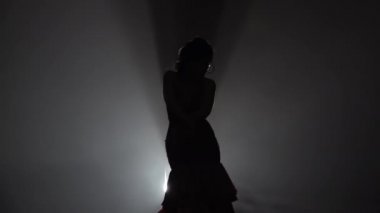 Kız elleri onun sırtına ile ayakta akan hareketleri dans ediyor. Arkadan ışık. Duman arka plan. Ağır çekim. Siluet