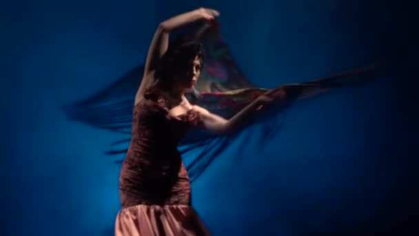 La mujer está bailando con un manto en sus manos. Luz por detrás. Fondo azul humo. Movimiento lento — Vídeo de stock