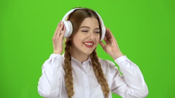 Flicka lyssnar på musik genom hörlurar. Grön skärm. Slow motion — Stockvideo
